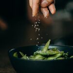 A hand sprinkles salt on fresh edamame, showcasing a delicious and healthy cooking moment.