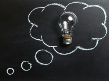 Light bulb laying on chalkboard with drawn thought bubble, symbolizing creative ideas.