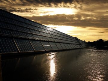 Silhouetted solar panels reflect sunset in tranquil waters, showcasing renewable energy.