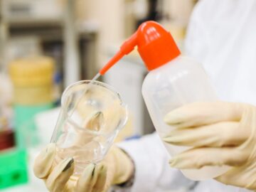 Scientist carefully pouring liquid into a beaker in a laboratory setting, wearing protective gloves.