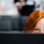 A woman with red hair intensely focused on a computer screen in an office setting.