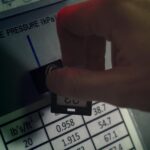 Close-up of hand adjusting pressure gauge dial in an industrial setting with visible pressure readings and controls.