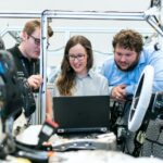 Engineers collaborating on a car project in a modern automotive workshop using advanced technology.