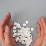 A close-up of hands surrounding white pills on a gray background, symbolizing medication and health concerns.