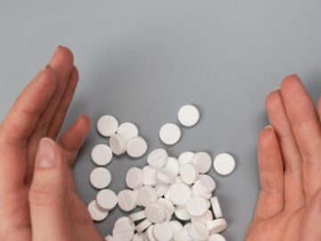 A close-up of hands surrounding white pills on a gray background, symbolizing medication and health concerns.