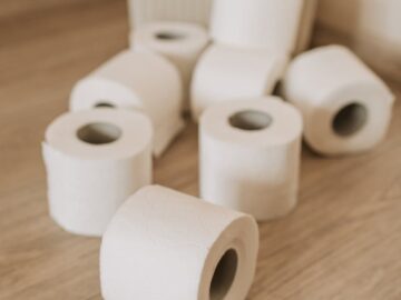 Multiple toilet paper rolls scattered on a wooden floor, highlighting hygiene essentials.