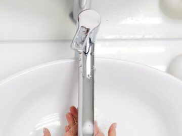 Hands washing under a sleek faucet with water flowing in a white basin