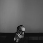 An Orthodox Jewish man with a beard and glasses, reading a book indoors.
