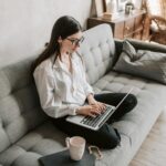 Woman in a cozy home setting working on a laptop for remote work and relaxation.