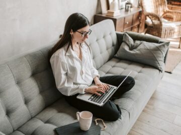 Woman in a cozy home setting working on a laptop for remote work and relaxation.