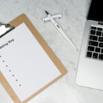 Flat lay of a wedding planning setting with clipboard, laptop, and pen.