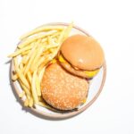 Two cheeseburgers and french fries served on a round plate against a white background.