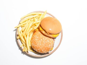 Two cheeseburgers and french fries served on a round plate against a white background.