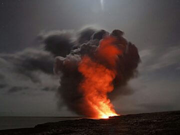 Volcanic eruption with smoke and lava under a starry night sky.