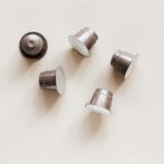 Minimalist photograph of several silver coffee capsules on a light background, perfect for coffee-related projects.