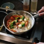 A chef cooks colorful vegetables in a skillet with butter on a stove in the kitchen.