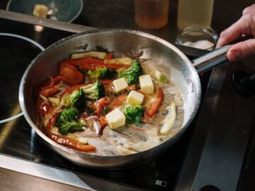 A chef cooks colorful vegetables in a skillet with butter on a stove in the kitchen.