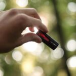 Close-up of a hand holding a USB drive outdoors with a bokeh background.