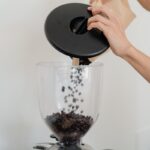 Close-up of hands pouring coffee beans into a grinder, preparing for a fresh brew.