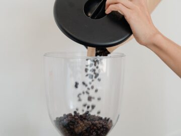 Close-up of hands pouring coffee beans into a grinder, preparing for a fresh brew.