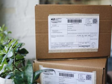 Close-up of shipping boxes with labels surrounded by houseplants indoors.