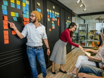Team members collaborating in a modern office with sticky notes on a wall, focusing on brainstorming and strategy.