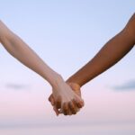 Closeup of multiracial hands holding, symbolizing unity and equality against a serene sky.