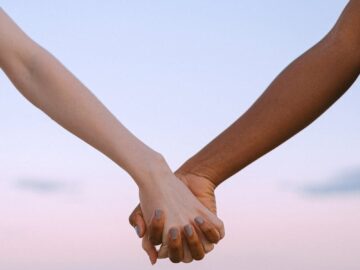 Closeup of multiracial hands holding, symbolizing unity and equality against a serene sky.