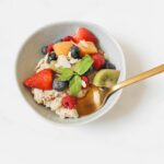 A nutritious bowl of oatmeal topped with fresh fruits and mint, presented with a golden spoon.