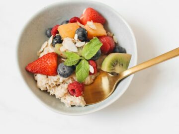 A nutritious bowl of oatmeal topped with fresh fruits and mint, presented with a golden spoon.