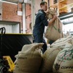 Warehouse employee handling burlap coffee sacks, industrial setting.