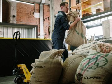 Warehouse employee handling burlap coffee sacks, industrial setting.