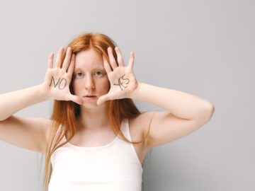 A young woman with red hair poses with 'No' and 'Yes' written on her palms, showcasing consent.