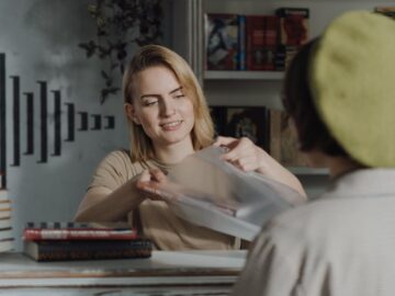 A cheerful female clerk helps a customer at a cozy bookstore counter.