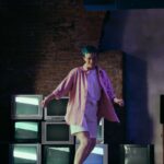 Teen girl with colored hair roller skating indoors near old CRT TVs, exuding fun and retro vibes.