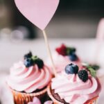 Delight in sweet pink cupcakes adorned with fresh berries and a heart topper, perfect for celebrations.