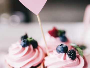 Delight in sweet pink cupcakes adorned with fresh berries and a heart topper, perfect for celebrations.