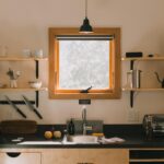 Modern kitchen interior with wooden shelves and hanging lamp above sink in light home