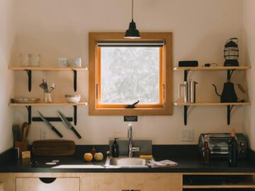 Modern kitchen interior with wooden shelves and hanging lamp above sink in light home