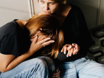 Two women sharing a comforting moment on a kitchen floor, depicting empathy and support.
