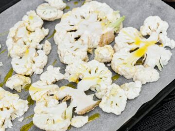 Sliced cauliflower with olive oil on a baking tray, perfect for a healthy meal.