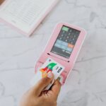 Close-up of hand swiping Visa card on pink POS machine for payment.