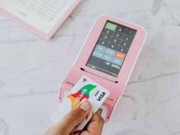 Close-up of hand swiping Visa card on pink POS machine for payment.