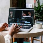 Freelance video editor working on a laptop in a cafe setting, utilizing Adobe software.