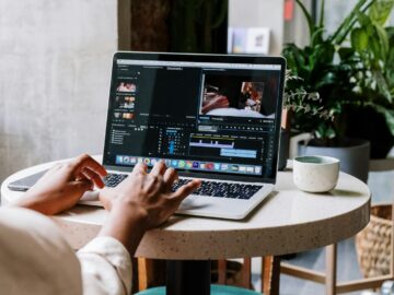 Freelance video editor working on a laptop in a cafe setting, utilizing Adobe software.