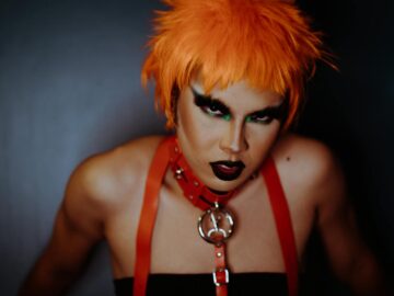 Striking portrait of a model with vibrant orange hair and dramatic makeup in a creative studio setting.
