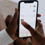 Hands holding a smartphone showing various apps including TikTok in a close-up view.