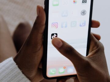 Hands holding a smartphone showing various apps including TikTok in a close-up view.