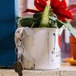A decorative mug holding red artificial flowers and a key indoors. Charming decor.
