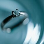 Close-up of a diamond engagement ring on a shimmering blue surface, evoking elegance and romance.